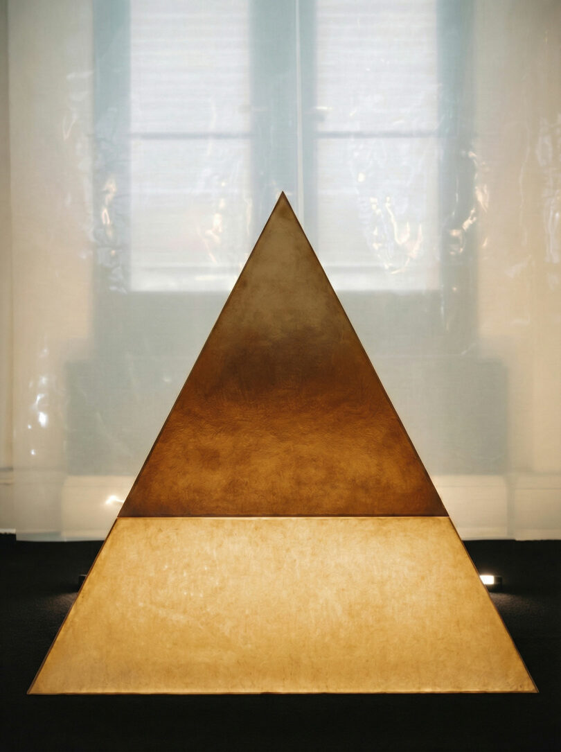 A triangular structure with a glowing ATRA base, set against a softly lit background with a window and translucent curtains.