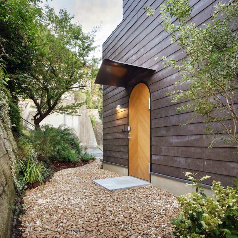 angled view of modern home exterior with dark siding and light wood front door