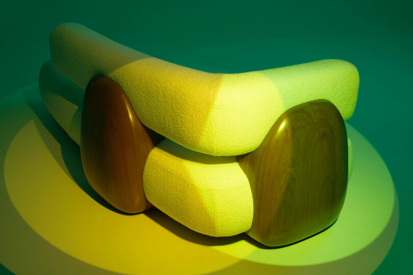 Curved, modern Holly Hunt sofa with cream textured upholstery and smooth wooden side panels, beautifully lit by green and yellow lighting.
