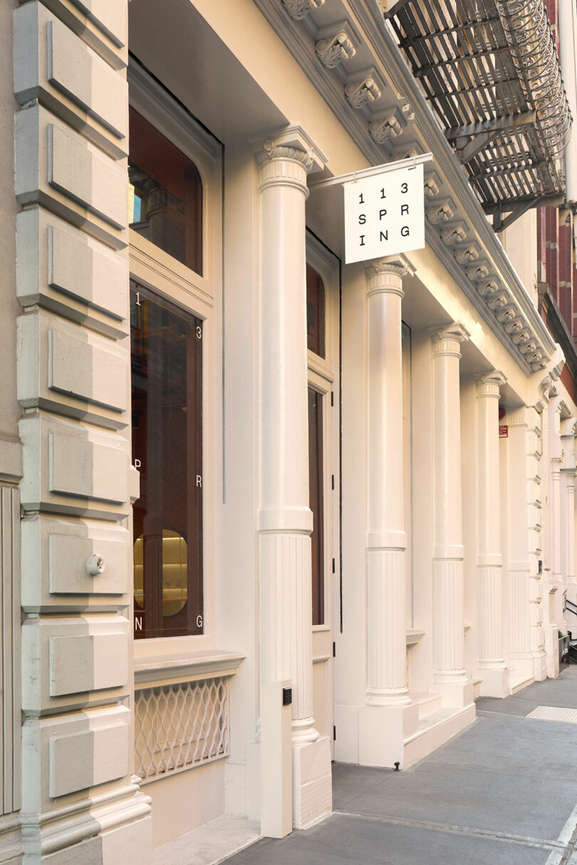 Facade of a cream-colored building with columns, large windows, and a sign that reads "113 SPRING" above the entrance.